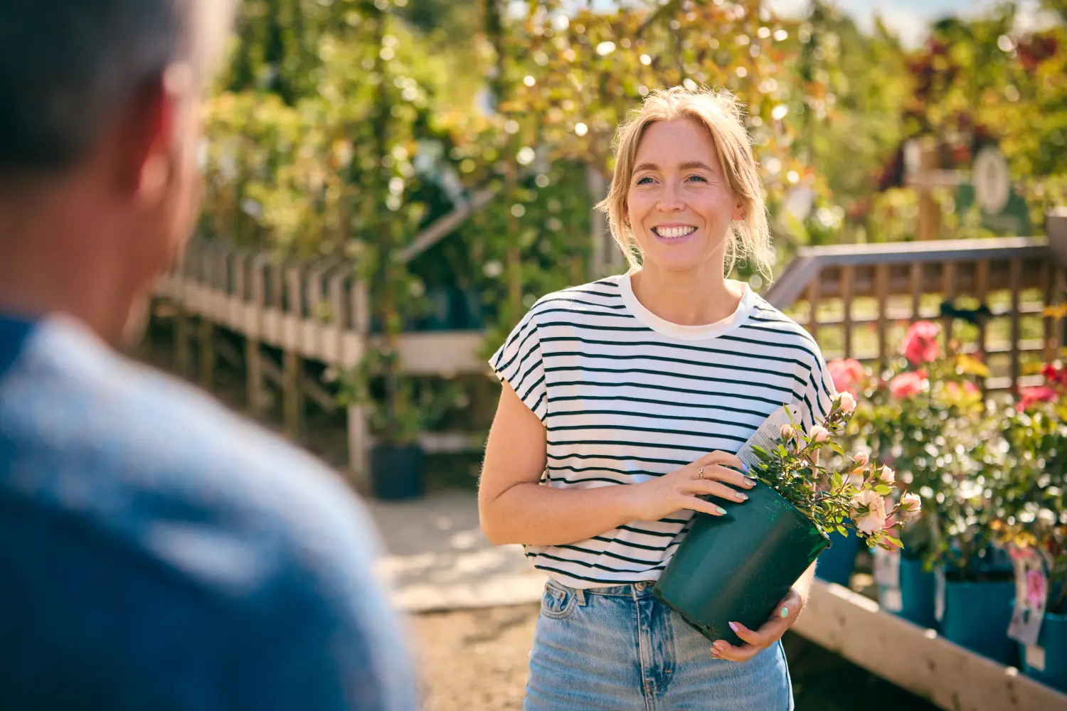 Frau im Gartencenter fragt Verkäuferin bei der Auswahl und dem Kauf einer Rose um Rat.